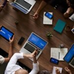 Overhead view of a diverse team discussing around a wooden table, using technology.